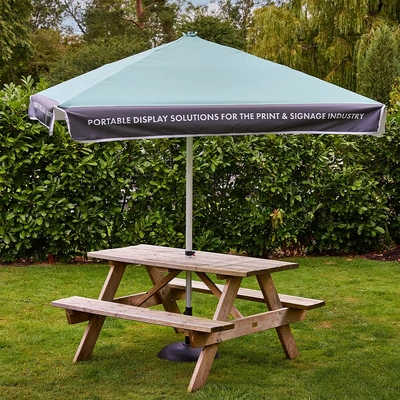 Example of a square printed parasol over an outdoor picnic table. Furniture is not included; base depends on the selected package.