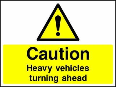 A black exclamation mark inside a yellow warning triangle above black wording on a yellow panel with Caution — Heavy vehicles turning ahead wording. CONS0104 artwork.