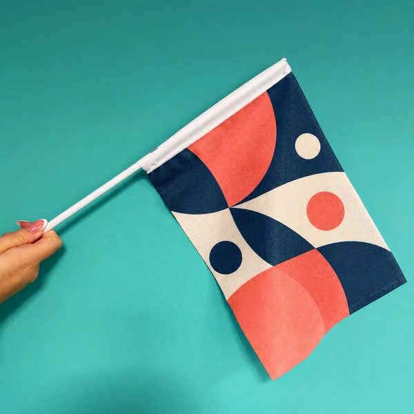 Illustrative product mockup of a hand waving flag with an unbranded geometric print in navy, coral and cream.